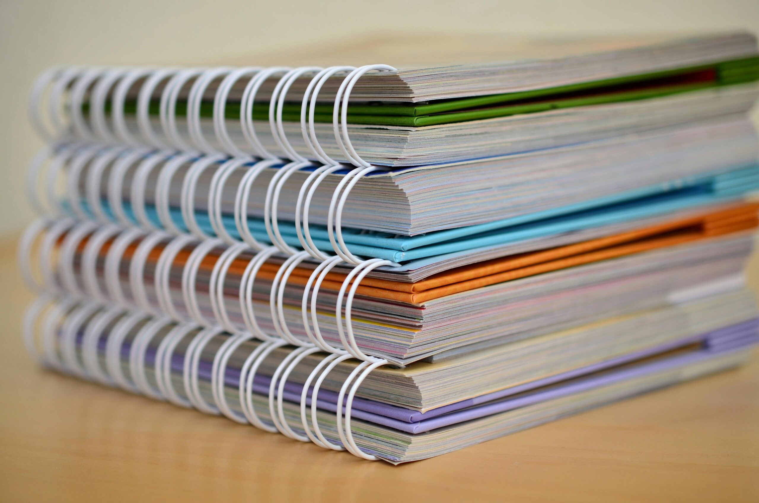 A colorful stack of spiral-bound notebooks neatly placed on a wooden desk. Ideal for educational themes.